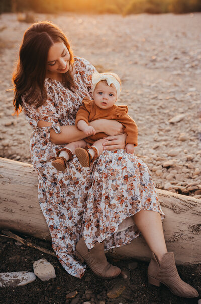 Golden hour family session with mother holding baby sitting on log