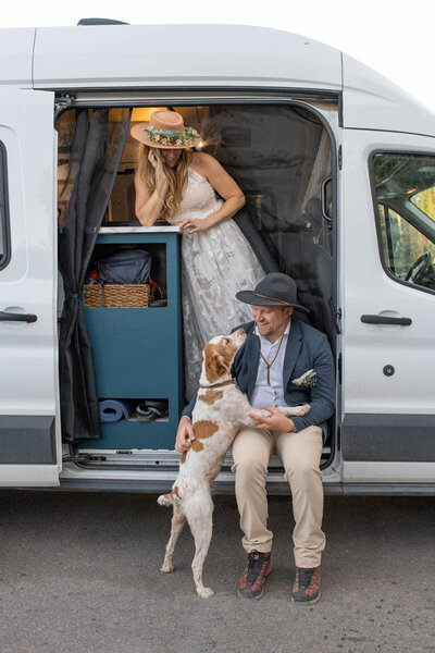 Bride and groom sit with their dog in camper van during elopement