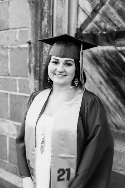 Girl wearing graduation cap and gown in front of rustic barn for Tacoma area senior portrait session