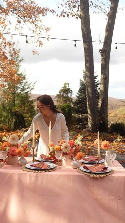 Wedding table styled with autumn florals and taper candles, with a planner adjusting details outdoors, designed by Yours Truly, a wedding planner and designer in New Jersey.