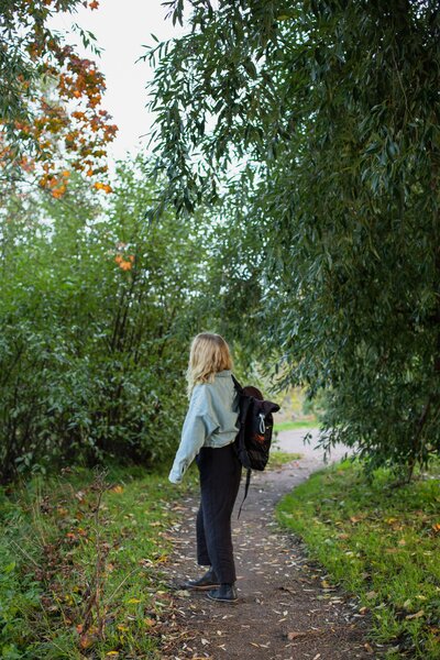 mielen paremminvoinnin ja kehomieliyhteyden valmentaja  kävelee metsätiellä puiden keskellä