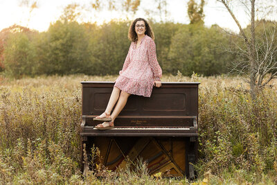 Girl sitting on a piano, outside in a field