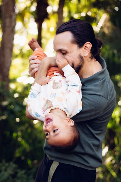 A father joyfully lifts his baby into the air, showcasing a moment of affection and playfulness between them.