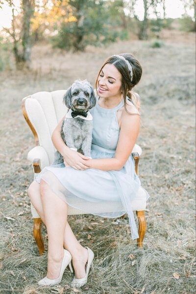 Kristen with fur-baby dog Rocko with bow-tie sitting in an armchair