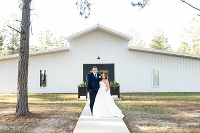 Bride and groom posing in front of The Grove with rustic barn in background.