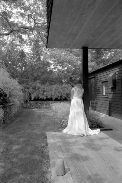 A woman in a wedding dress stands gracefully on a porch, radiating joy and elegance on her special day.