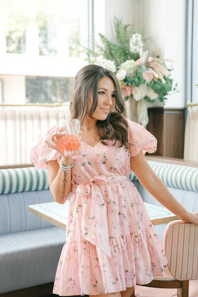 Cassie Loree posing in a pink dress and holding a drink