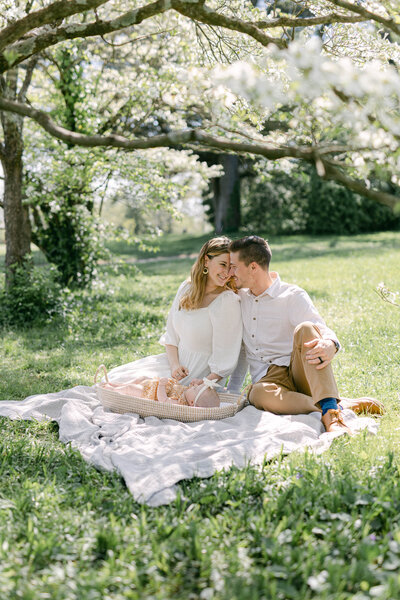 knoxville family photographer. husband and wife sitting under dogwood blooms with baby girl laying in basket in front of them