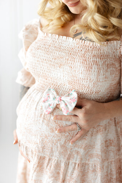 Mom holding a sweet little bow on her belly and loving on her little girl