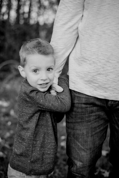 Black and white photo of toddler boy hugging his dad’s hand in Gambrills Maryland
