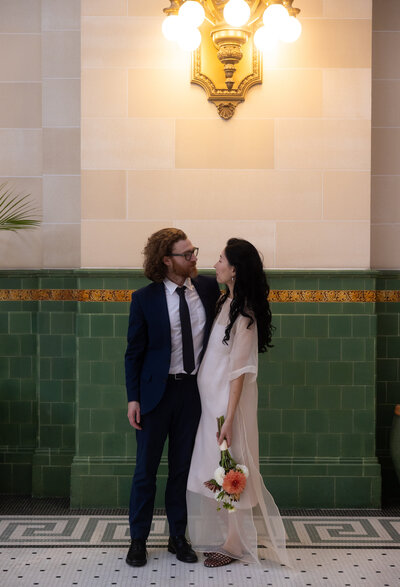 Couple glancing at each other at the Union station as the woman holds a bouquet of vibrant flowers in her sheer white dress and man wears a tuxedo 