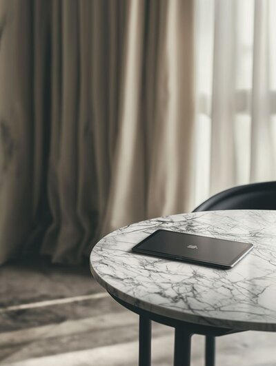 Closed black tablet resting on a round marble table in a softly lit room with neutral curtains