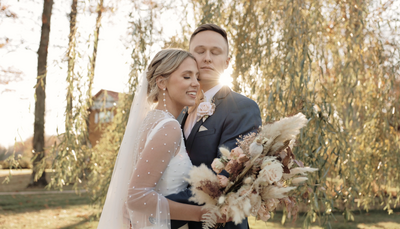 Bride and groom stand under willow tree at the Willow Lake Event Center