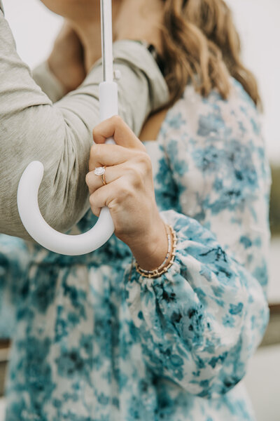 Close up of woman's hand holding an umbrella while her fiancé holds her face, the focus on her engagement ring.