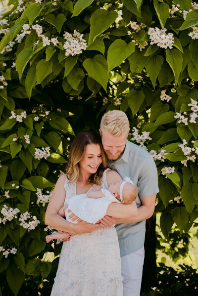parents holding their newborn baby girl in front of flowery tree at the Arboretum