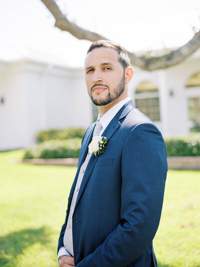 groom in a navy blue suit stands tall outside of a white chapel in St. Petersburg Florida