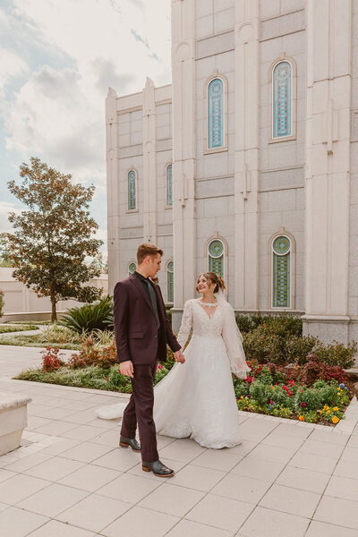 Bride and groom walking hand in hand outside the LDS Houston Temple in Texas, with the stunning white architecture as a backdrop during their elegant wedding day.
