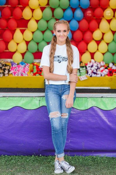 high school senior girl shigh school senior girl sitting  in front of ballon pop game at wayne county ohio fair photographed by Jamie Lynette Photography Canton Ohio Senior Photographer