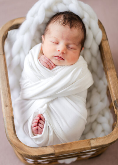 Sleeping newborn baby posed on pink background in a wooden basket prop at Allison Reilly's Union County, NJ photo studio.