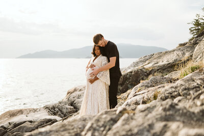 A photo of a couple embracing on a rock in front of the Ocean at Lighthouse Park in West Vancouver.