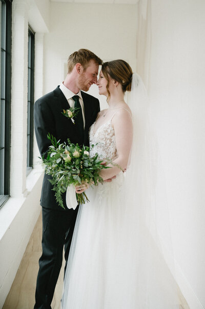 Indoor wedding ceremony at The Arbor Loft, featuring whitewashed brick walls, hanging greenery, and guests seated in rows.