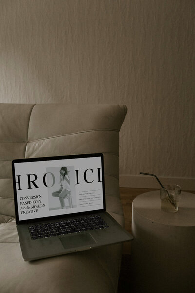 Minimal warm beige and white living space featuring a soft couch, a drink with a straw on a table, and laptop with a mockup of a website