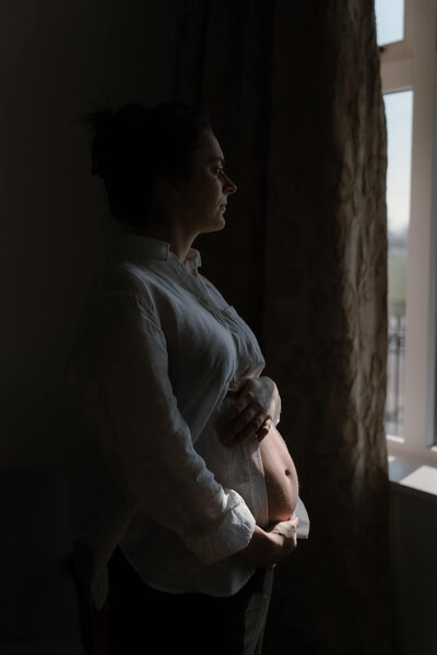 zwangere vrouw kijkt naar buik tijdens zwangerschapsshoot, gefotografeerd door familiefotograaf Julia de Groot