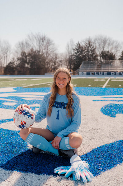 High school soccer player sits on the field ball in hand.