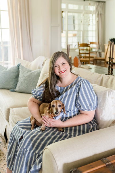 Lauren sits on her family room sofa holding her mini dachshund