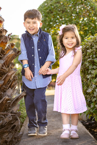 Big brother hugging his little sister as they smile among blooming roses, taken by a Bay Area family photographer.