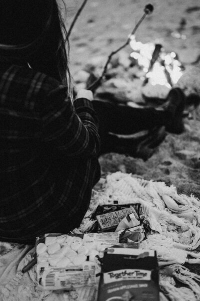 black n white close up of the gram crackers & marsmellows as B in the background puts her s'mores over the campfire on the beach