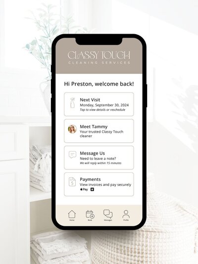 A phone mockup of the Classy Touch Cleaning client app, showing features like visit scheduling, messaging, payments, and a warm welcome from “Tammy”—against a backdrop of a clean, folded-linen laundry scene.