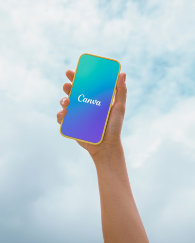 A hand holding a bright blue and yellow smartphone displaying the distinct Canva logo on its screen, set against a light blue background, representing the powerful graphic design capabilities of Canva Pro.