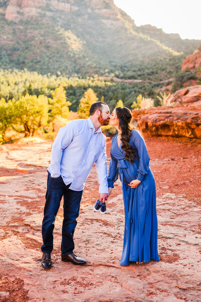 Sedona red rocks couple holding baby shoes kissing