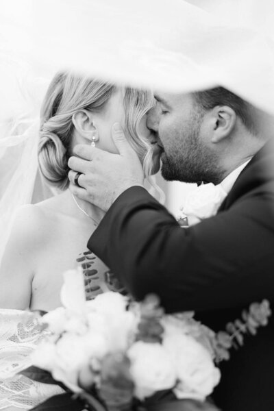 Black and white image of a couple kissing passionately under a veil