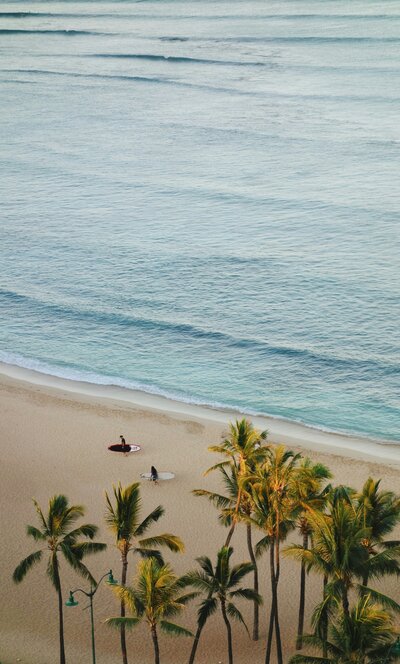 Two surfers walking in the sand next to a blue ocean