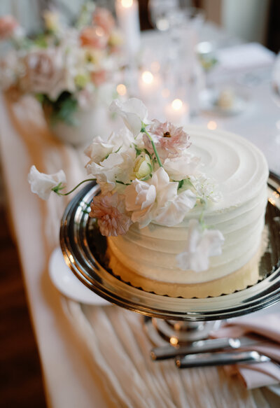 A photo of a wedding cake with pink and white fresh flowers on top