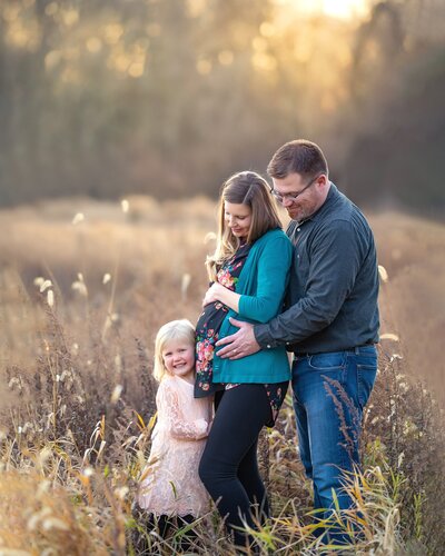 family of three smiling at mom's belly