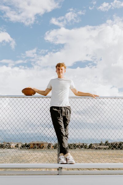 Christian poses for a sports themed senior shoot while holding a football.