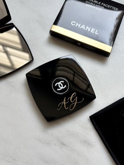 Personalized black Chanel compact mirror with initials in gold engraving.