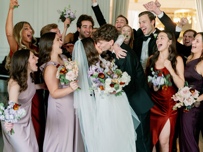 Bride and groom kissing surrounded by cheering wedding party
