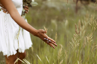 hand with silver rings softly touching tall grass in a field