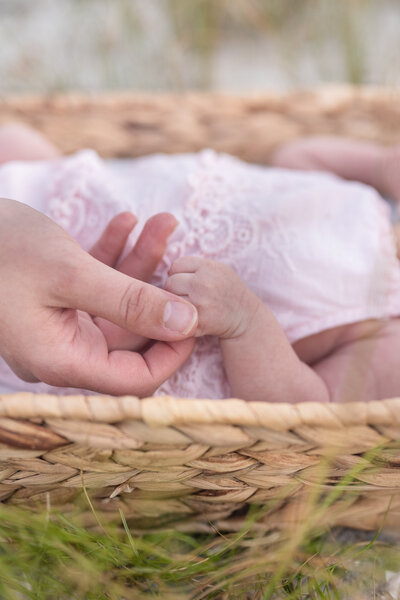 mother holding hand of newborn baby wearing pink lace in a tan basket in holly ridge, north carolina