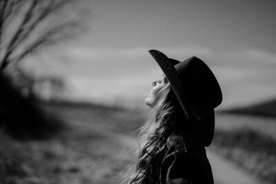 Woman poses in the sunlight in  a black cowboy hat.