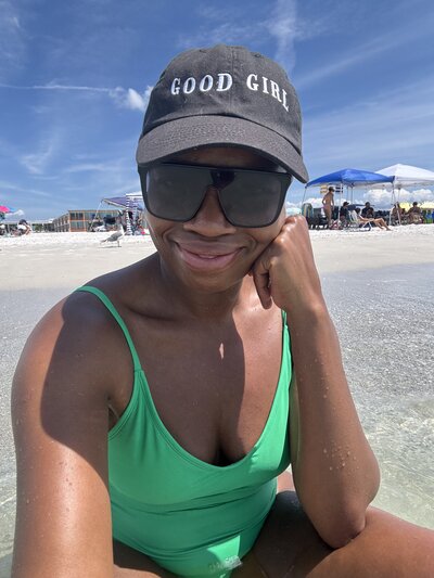 Black career coach for women in green swimsuit wearing black cap at beach
