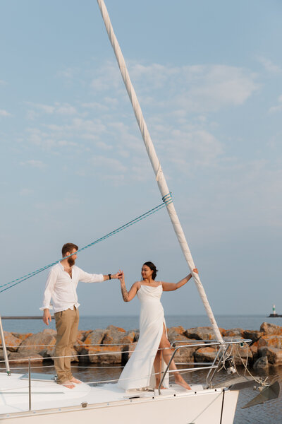 A couple holding hands as they stand at the front of a sailboat 