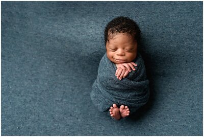 A newborn baby boy wrapped in a blue wrap with toes and hands out .