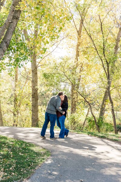 Couple kissing on a path underneath fall trees