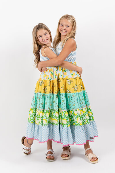 2 sisters embrace in matching sundresses and smile