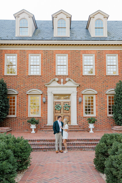 Engaged couple smiling at one another in front of estate
